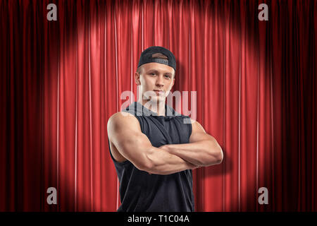 Jeune homme musclé en vêtements de sport noir sur fond rouge des rideaux de scène Banque D'Images