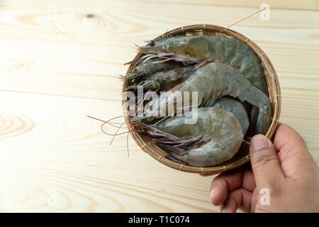 Les mains des hommes sont holding group de matières premières fraîches crevettes blanches du Pacifique en bambou bol sur table en bois. Banque D'Images