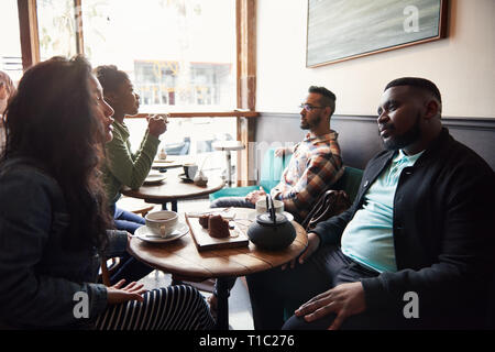 Divers amis parler ensemble autour d'un café dans un café Banque D'Images