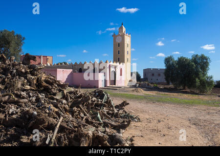 Pile de diverses pièces d'un bois. Mosquée avec nouvelle façade à l'arrière-plan. Pentagramme marocain sur la tour. Ciel bleu avec des nuages blancs. Maroc Banque D'Images