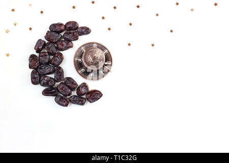 Ramadan, l'iftar la composition du bureau. Fruits secs date disposés en forme de lune bronze, café, thé tasse et étoiles confettis sur fond blanc. Cuisine de fête Banque D'Images