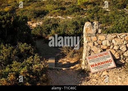 Un signe avec un avertissement pour les visites de touristes, à ne pas obtenir trop près du bord de la falaise, couché à côté d'ancien mur de pierre. Chemin entre les petits arbustes Banque D'Images