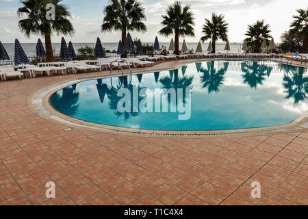 Piscine vide pendant un peu de nuages pendant la journée pendant les vacances d'été. Voir d'eau bleue dans la piscine, transats, parasols, palmiers, d'horizon et la mer à l'arrière Banque D'Images