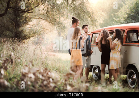 Un groupe d'amis debout à l'extérieur sur un roadtrip à travers campagne, à boire. Banque D'Images