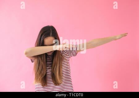 Portrait de jeune fille brune faisant geste danse dab sur fond rose. Concept de vie Banque D'Images