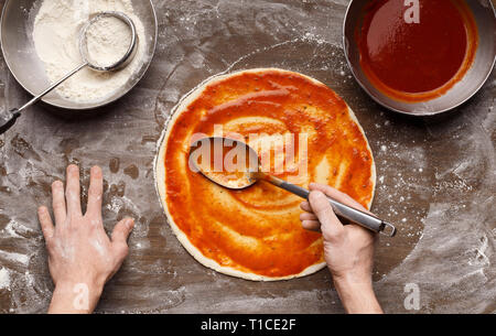 Répandre la sauce tomate sur la pizza pour la cuisson de base et prepering Banque D'Images