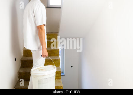 Peintre l'homme au travail avec un seau de peinture blanche debout à faire les escaliers maison rénovation Banque D'Images