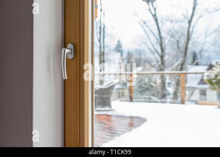 Vue de la chambre à travers un balcon fermé avec une poignée de fenêtre sur une terrasse avec une chaise en osier et d'une balustrade. Banque D'Images