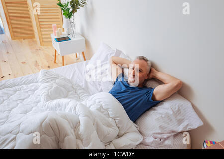 Homme aux cheveux gris barbu au frais dans son lit pendant le week-end. Banque D'Images