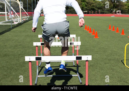 Un athlète masculin de l'école plus de sauts d'obstacles au cours de l'entraînement musculaire pour la pratique de l'athlétisme Banque D'Images