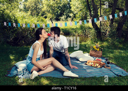 Jeune couple sur un pique-nique dans un parc de la ville assis sur une couverture elle s'embrasser son nez rouge de clown, Selective focus Banque D'Images