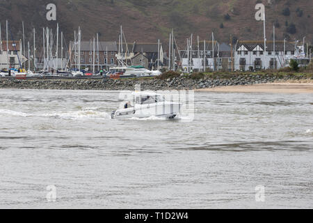 Lieu de loisirs à moteur de faire son chemin jusqu'à l'estuaire de Conwy la mer ouverte avec le port de plaisance de Conwy dans l'arrière-plan Banque D'Images