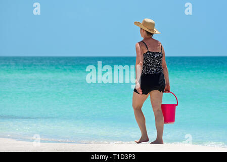 Femme marche sur Gulf Coast Beach en Floride portant un seau de plage rouge Banque D'Images