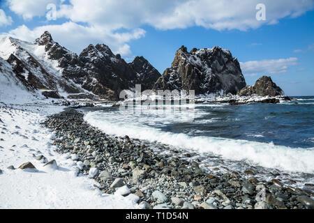 Des roches couvertes de neige et de la mer sur les piles de la mer du Japon en hiver sur Hokkaido. Les vagues déferlent sur le rivage rocailleux, et la neige recouvre une grande partie de la scène. Banque D'Images