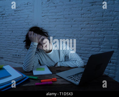 Surmené et fatigué étudiante travaillant tard dans la nuit sur l'ordinateur portable en essayant de ne pas s'endormir et faire un effort pour se concentrer et continuer à étudier Banque D'Images