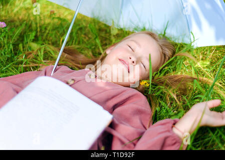 Petite fille s'endormit avec un livre dans le parc à l'herbe sur la pelouse Banque D'Images