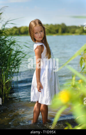 Jolie petite fille en robe blanche debout dans l'eau des Banque D'Images