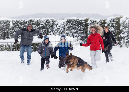 S'amuser en famille dans la neige profonde, fonctionnant avec leur berger allemand. Banque D'Images