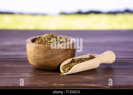 Lot de graines de cumin romain avec bol en bois avec champ de blé vert Banque D'Images