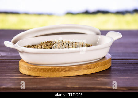 Lot de graines de cumin romain dans une cocotte en céramique avec champ de blé vert Banque D'Images