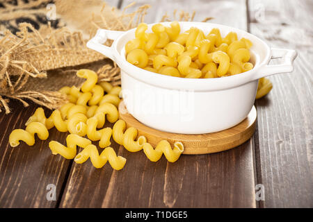 Beaucoup de pâtes cavatappi ensemble dans une cocotte en céramique dans un sac de jute sur bois marron foncé Banque D'Images