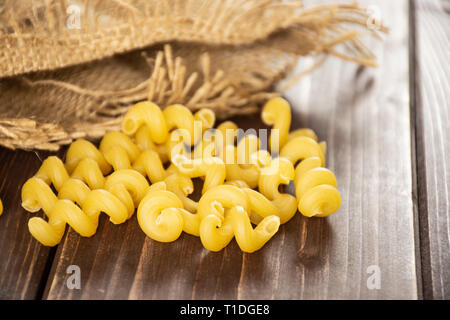 Beaucoup de pâtes cavatappi ensemble dans un sac de jute sur bois marron foncé Banque D'Images