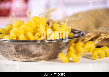 Beaucoup de pâtes cavatappi ensemble dans le vieux bol de fer dans un sac de jute dans une cuisine blanche Banque D'Images