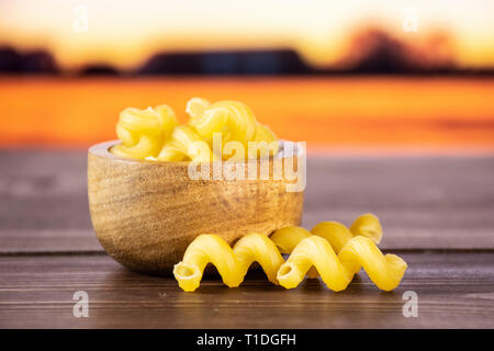 Lot de pâtes crues cavatappi avec bol en bois avec champ d'automne en arrière-plan Banque D'Images