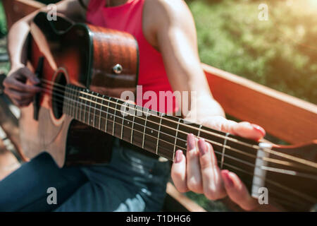 Close up des mains du musicien jouant de la guitare. Fille est maintenant ses doigts sur les cordes de la guitare. Fille est assis sur un banc à l'extérieur dans cette belle Banque D'Images