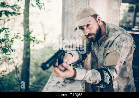 Homme courageux et concentré est debout près de la sortie et la tenue d'arme dans ses mains. L'homme est maintenant doigt sur la gâchette. Mercenaire est calme. Il est en attente. Banque D'Images