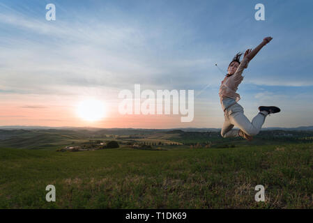 Concept de la liberté. Une femme de sauter devant un magnifique paysage de Toscane au coucher du soleil, se sentir heureux et la liberté Banque D'Images