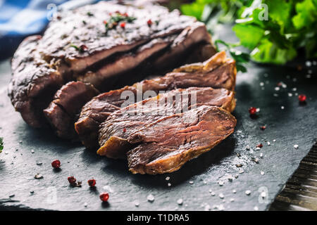 Pavé de boeuf grillé fraîchement sur ardoise plaque avec sel poivre et persil romarin herbes. Fabricants de pièces de bœuf juteux Banque D'Images