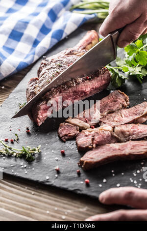 Tomahawk fraichement grillés steak sur ardoise plaque avec sel poivre et persil romarin herbes. Chef avec entaille bovine juteux steak Banque D'Images