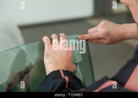 L'assistant d'installation d'équipement supplémentaire bois une teinte film sur le côté de la vitre avant de la voiture et l'arrêt de la partie excédentaire à l'aide d'un couteau Banque D'Images