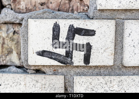 Close-up swastika nazie panneau noir peint sur vieux mur de briques gris en ruine . Banque D'Images