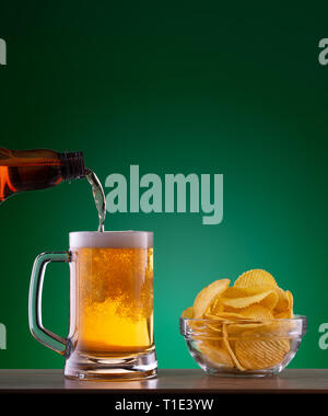Plaque avec chips et bière légère verser dans la tasse sur fond vert Banque D'Images