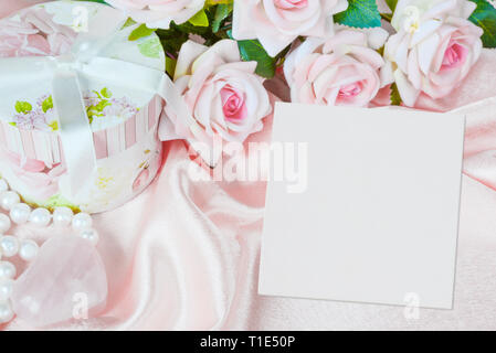 Des roses rose, boîte cadeau ronde, carré blanc feuille de papier vierge ou toile et un collier de perles sur un tissu de soie, rose de la composition avec copy-space Banque D'Images