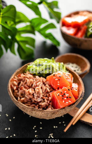 Bol avec Poke Poisson saumon cru, salade chuka et le riz dans des bols de coco sur fond noir Banque D'Images