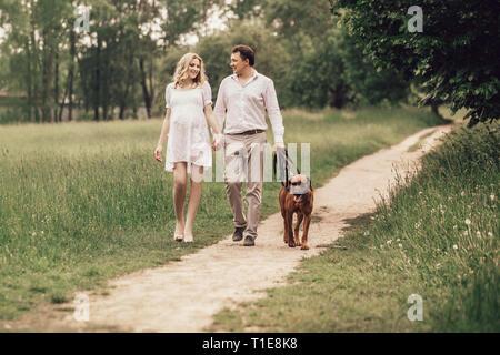 Beau mari et sa femme enceinte avec leur chien sur une promenade dans le parc Banque D'Images
