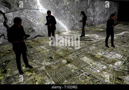 Berlin, Allemagne. Mar 25, 2019. Les gens marchent avec bacs sur une photographie aérienne de Berlin, marquant le tracé du mur et les lieux liés à la Stasi. Le spectacle avec le titre 'Stasi à Berlin - La surveillance et la répression dans l'Est et l'Ouest' affiche l'infrastructure cachés de la Stasi et sera ouverte le 28 mars 2019 dans la Hohenschönhausen Memorial. (Pour dpa 'Nouvelle exposition : les réunions de la Stasi, Photo aérienne, des comprimés) Credit : Britta Pedersen/dpa-Zentralbild/dpa/Alamy Live News Banque D'Images