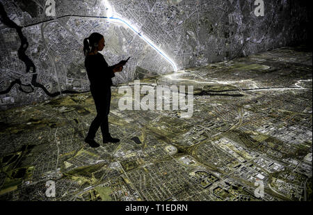 Berlin, Allemagne. Mar 25, 2019. Une jeune femme marche avec une tablette graphique sur une photographie aérienne de Berlin, marquant le tracé du mur et des lieux qui avait à voir avec la Stasi. Le spectacle avec le titre 'Stasi à Berlin - La surveillance et la répression dans l'Est et l'Ouest' affiche l'infrastructure cachés de la Stasi et sera ouverte le 28 mars 2019 dans la Hohenschönhausen Memorial. (Pour dpa 'Nouvelle exposition : les réunions de la Stasi, Photo aérienne, des comprimés) Credit : Britta Pedersen/dpa-Zentralbild/dpa/Alamy Live News Banque D'Images