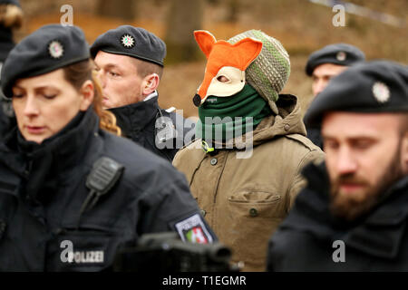 26 mars 2019, Berlin, Düsseldorf : Un homme dans un masque va à un véhicule d'urgence avec la police pour vérifier ses données personnelles. Au cours de l'opération policière pour une suspicion d'excréments dans le lanceur de Hambach forêt, une personne en cordée vers le bas d'une maison de l'arbre. Un porte-parole de la police a déclaré mardi qu'elle avait été prise d'une voiture de police pour déterminer ses coordonnées personnelles. Photo : David Young/dpa Banque D'Images