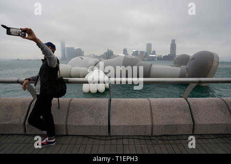 Hong Kong, Chine. Mar 26, 2019. Un visiteur prend une photo de lui avec le KAWS:MAISON DE VACANCES sur l'écran d'installation dans le port de Victoria de Hong Kong. Le KAWS:Maison de vacances structure élargie par l'artiste américain Brian Donnelly, également connu sous le nom de KAWS, sera à l'affiche jusqu'au 31 mars 2019. Crédit : Christopher Jue/ZUMA/Alamy Fil Live News Banque D'Images