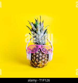 La mode à la mode des fruits ananas au casque et lunettes de soleil et d'écouter la musique sur fond jaune pastel. Hipster avec ananas frais Banque D'Images