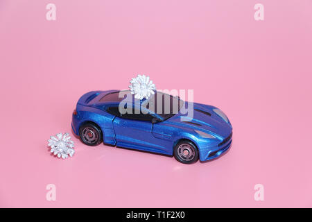 La voiture de sport bleu porte une fleur de cristal. Le cadeau se trouve sur le toit de la voiture. Fond rose. Jouet pour enfants. Il n'y a pas de gens. Banque D'Images