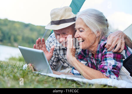 Happy senior couple in tent with tablet computer s'amuse à video chat Banque D'Images