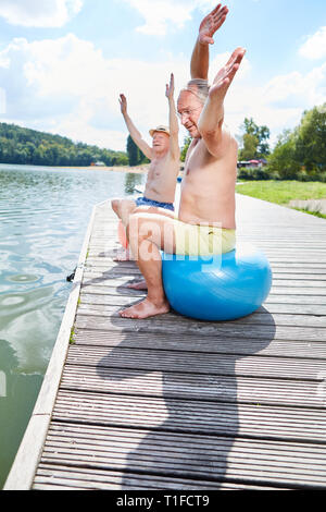 Deux personnes âgées avec ballon de gymnastique faire la gymnastique au lac en été Banque D'Images