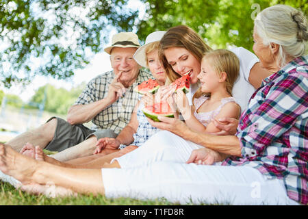 Famille élargie avec les grands-parents et la fille de manger dans le parc de détente de melon Banque D'Images