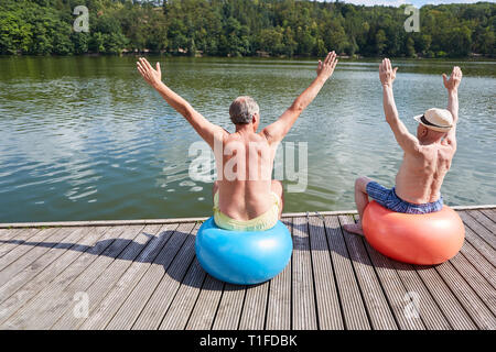 Deux aînés avec ballon de gymnastique ne retour exercices sur le lac en été Banque D'Images
