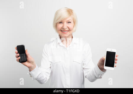 Happy senior man holding est un ancien téléphone avec des boutons et un nouveau téléphone avec un grand écran. Elle permet d'utiliser les deux de ces téléphones mais elle préfère appeler Banque D'Images